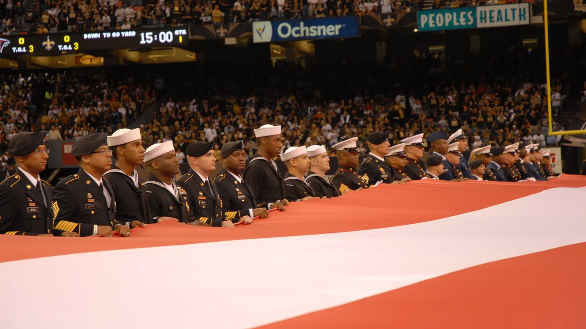 Militares seguram uma grande bandeira dos Estados Unidos diante das arquibancadas