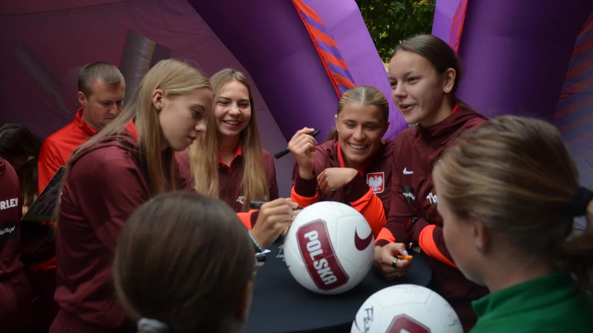 Jogadoras da seleção feminina sub-20 da Polônia autografam bolas diante de jovens torcedoras.
