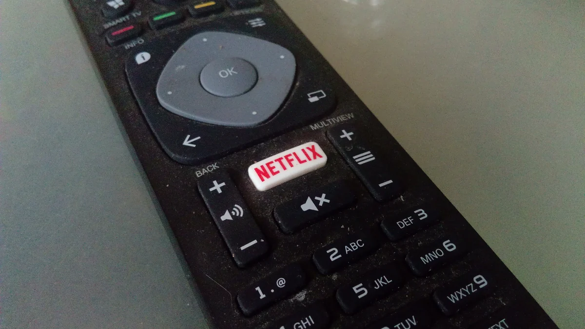Controle remoto preto com botão branco da Netflix entre teclas numéricas e de volume