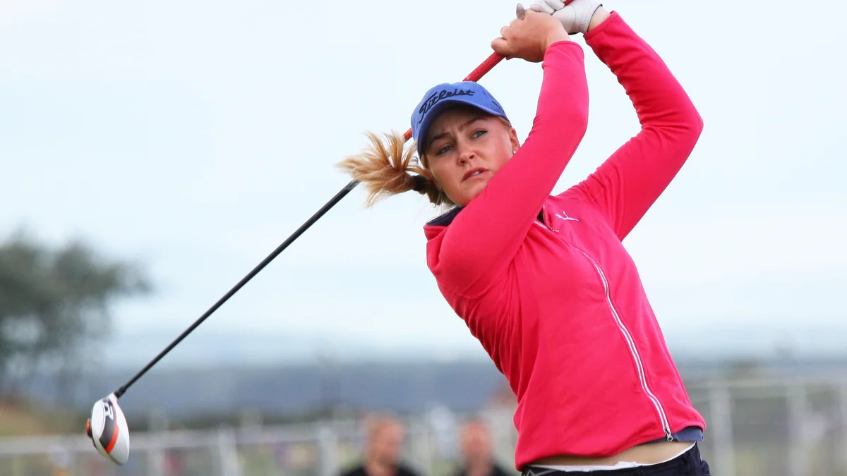 Charley Hull, in a pink jacket and blue cap, completes a golf swing with the club above her head.