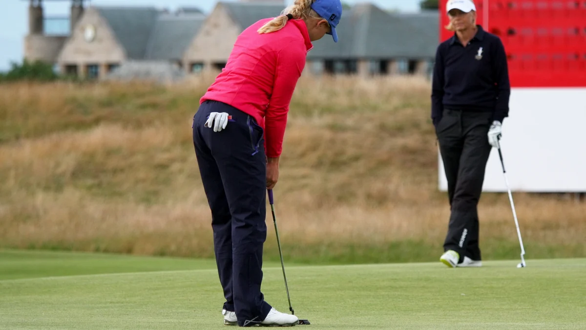 Charley Hull bends to play a putt on the green while another golfer watches in the background.