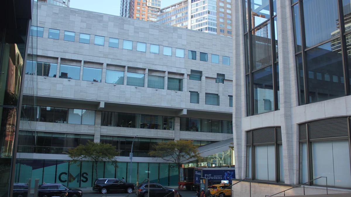 Stone and glass façades at Lincoln Center seen from the street, with cars in the foreground