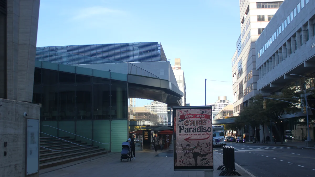Glass entrance beside Hearst Plaza, with a Café Paradiso sign on the sidewalk