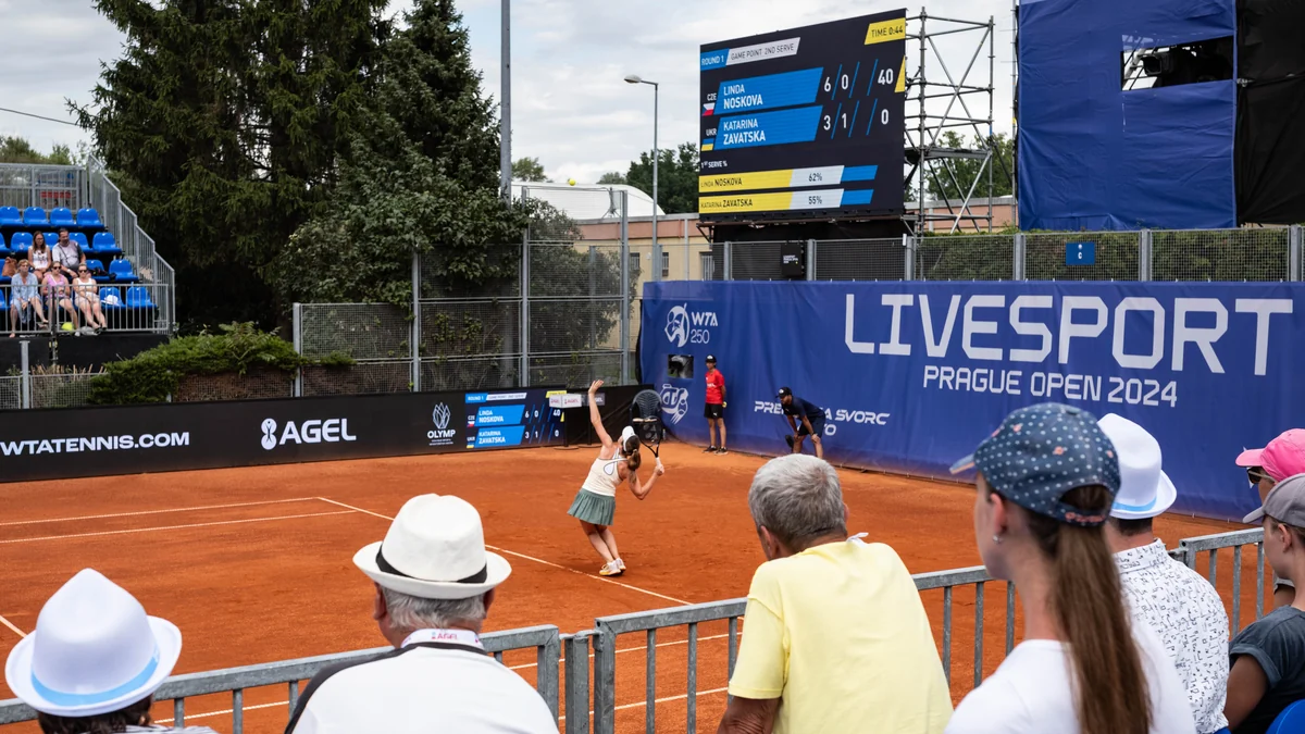 Linda Nosková saca em quadra de saibro diante de arquibancada e placar no Prague Open