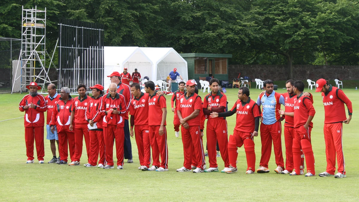 Jugadores y miembros de la selección de Omán vestidos de rojo y alineados en un campo de críquet