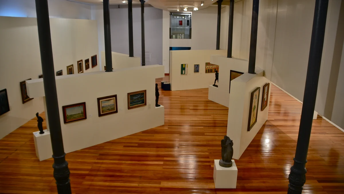 Upper-level view of galleries with white partitions, dark columns, paintings and sculptures on a wooden floor