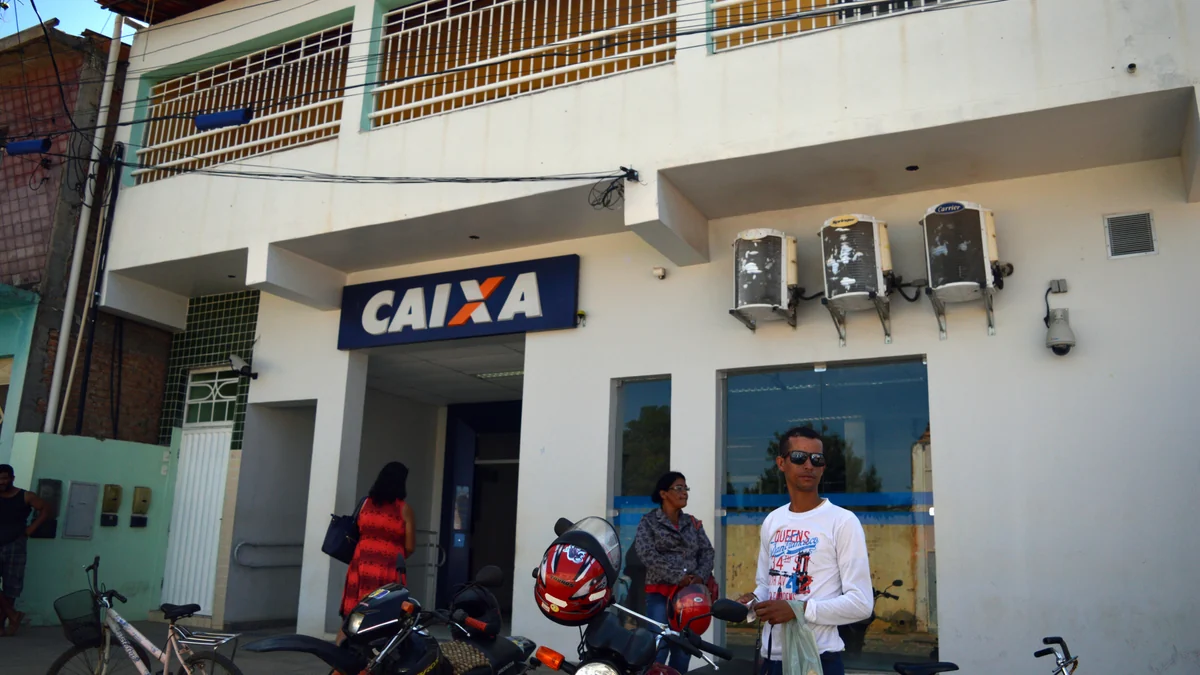 Exterior of a Caixa branch, with people, motorcycles, and a bicycle in front.