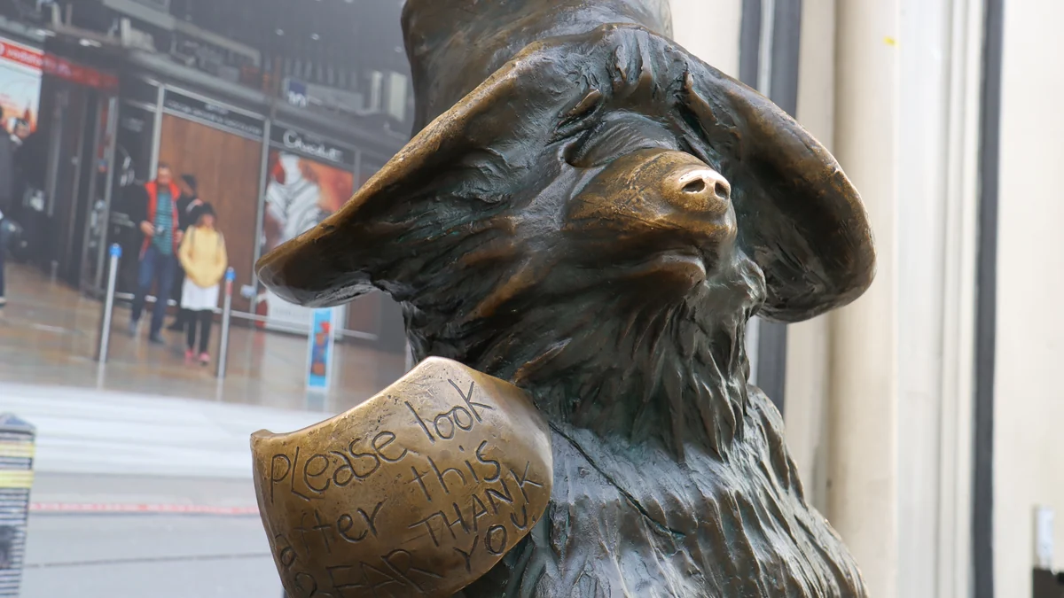 Gros plan de la statue de Paddington avec son chapeau et son étiquette en bronze devant une fenêtre