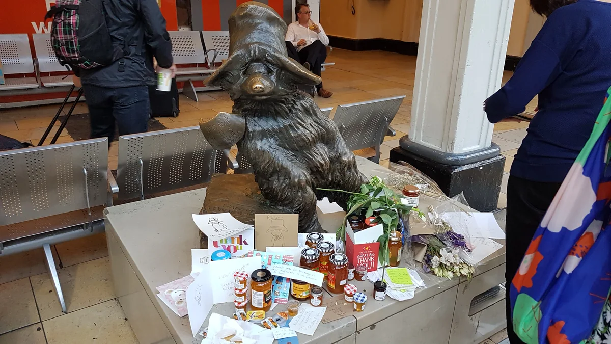 Statue en bronze de l’ours Paddington entourée de fleurs, de cartes et de pots de marmelade dans la gare
