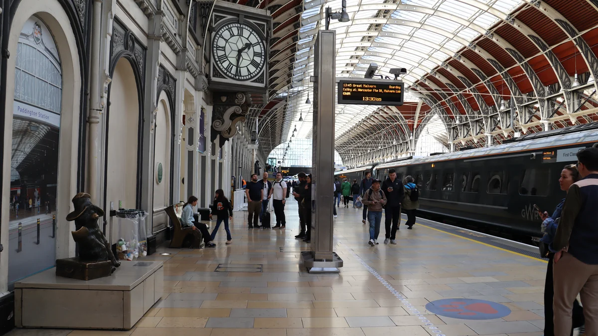 Quai couvert de la gare de Paddington avec la statue de l’ours à gauche, une horloge, un train et des voyageurs