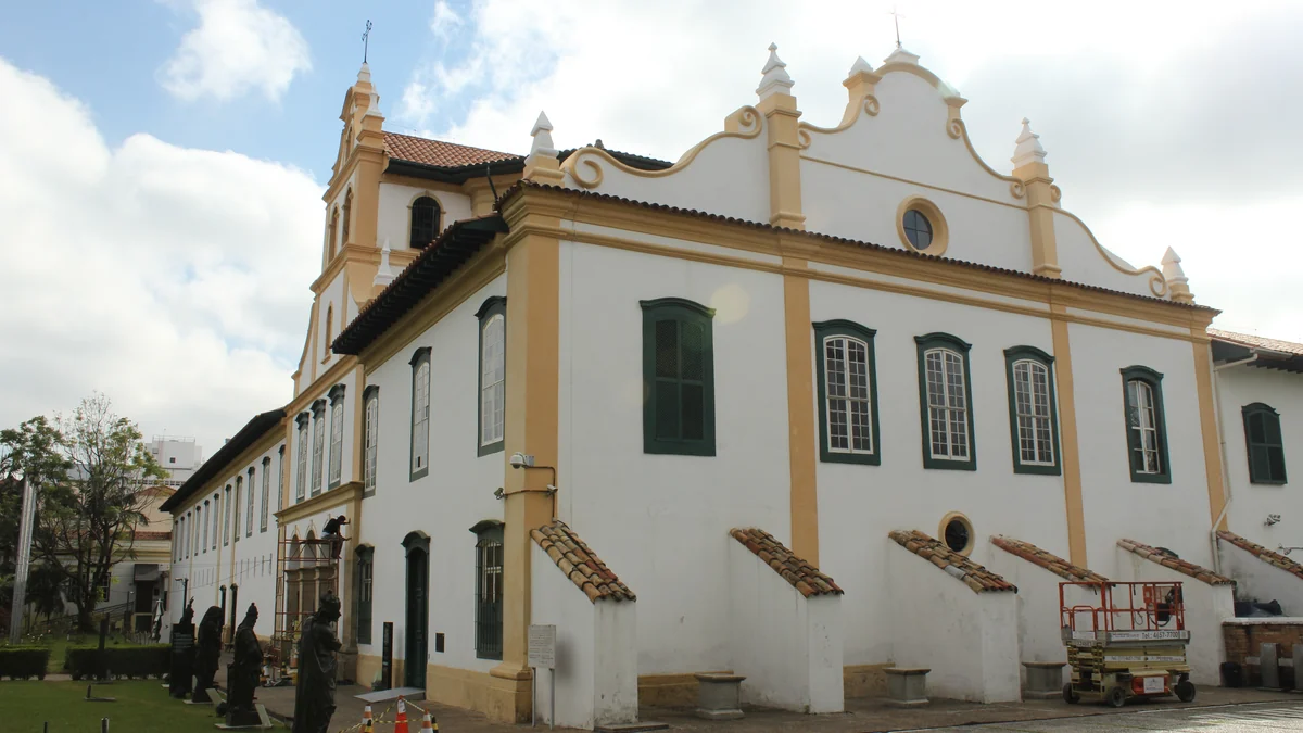 Fachada branca e ocre do Mosteiro da Luz, com janelas verdes e telhados de cerâmica