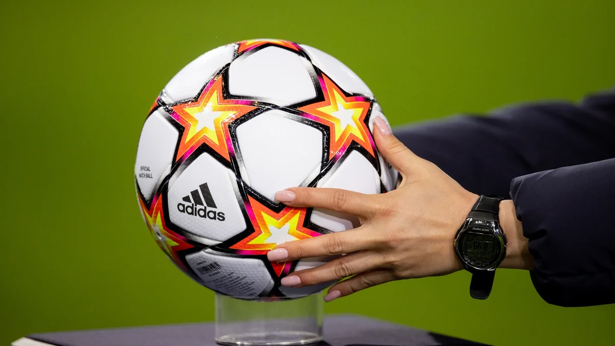 Une main tient un ballon blanc orné d'étoiles orange et noires devant un fond vert.