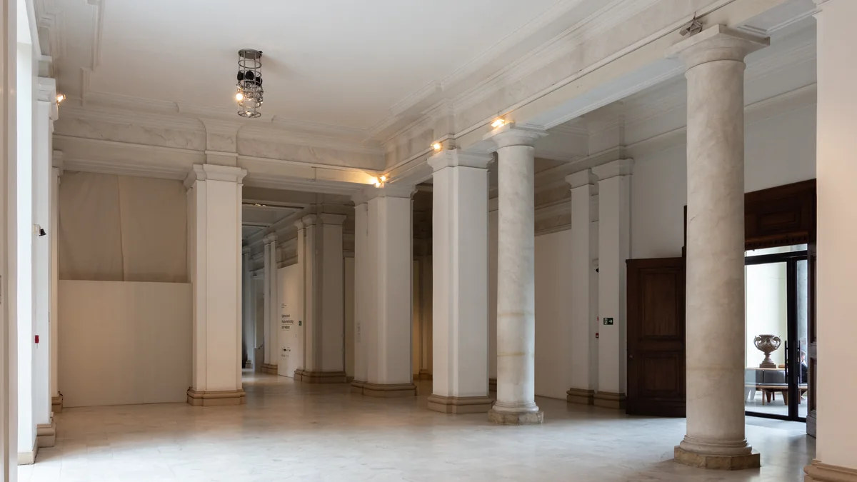 Galeria clara da Pinacoteca com colunas brancas, portas de madeira e iluminação no teto