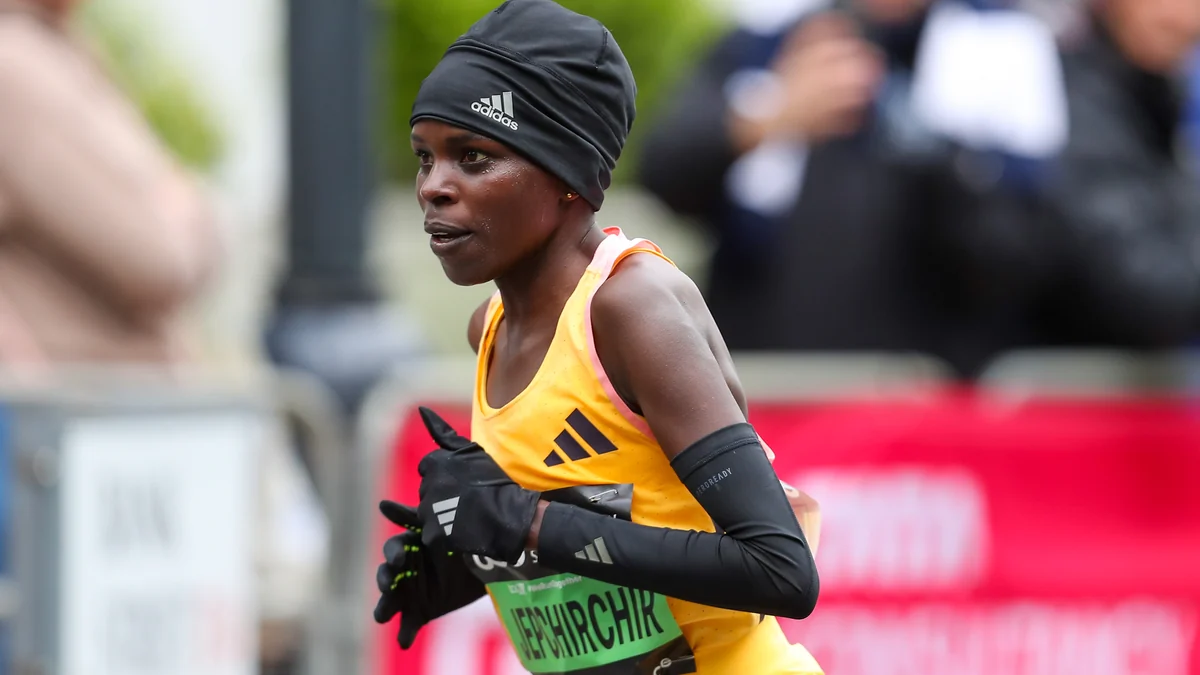 A runner in a yellow top, black cap, gloves and black arm sleeves during a road race.