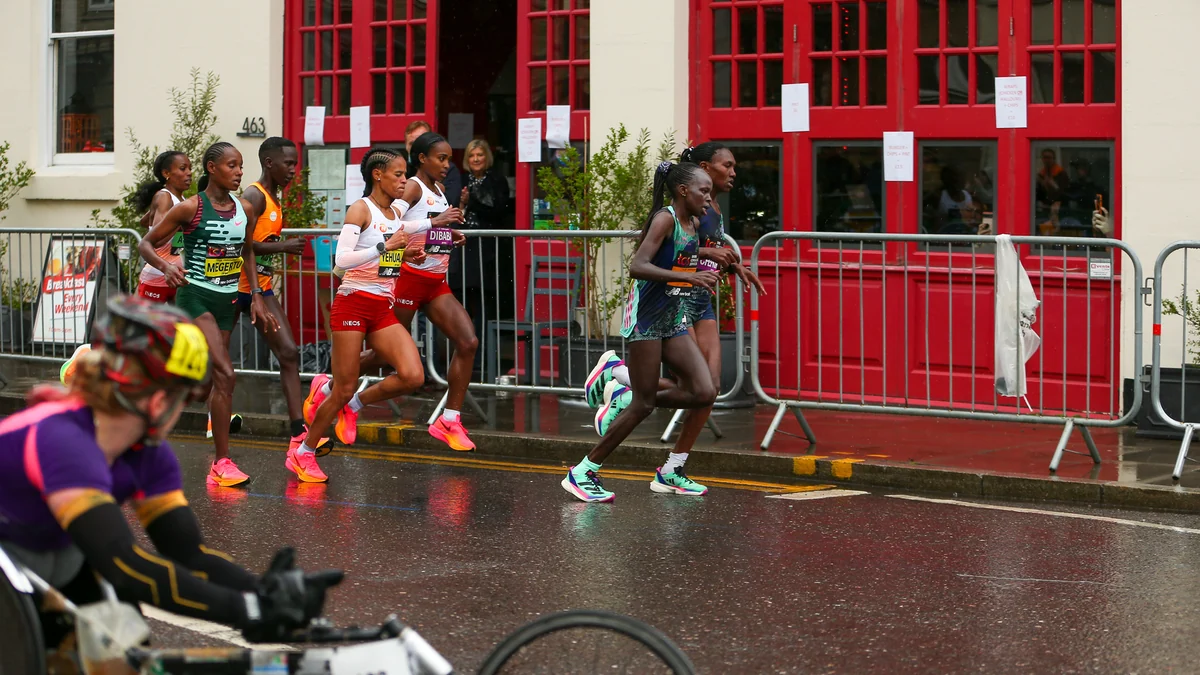Elite women runners pass a building with red doors on a wet street.