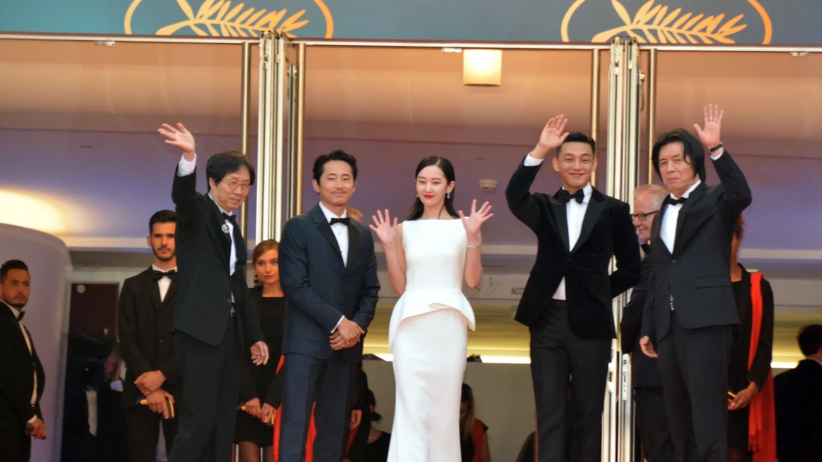 Lee Chang-dong e quatro integrantes de uma equipe de cinema posam em trajes de gala diante do emblema de Cannes.
