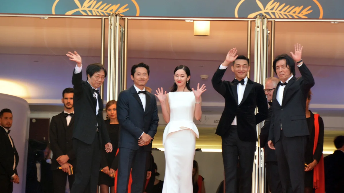Lee Chang-dong e quatro integrantes de uma equipe de cinema posam em trajes de gala diante do emblema de Cannes.