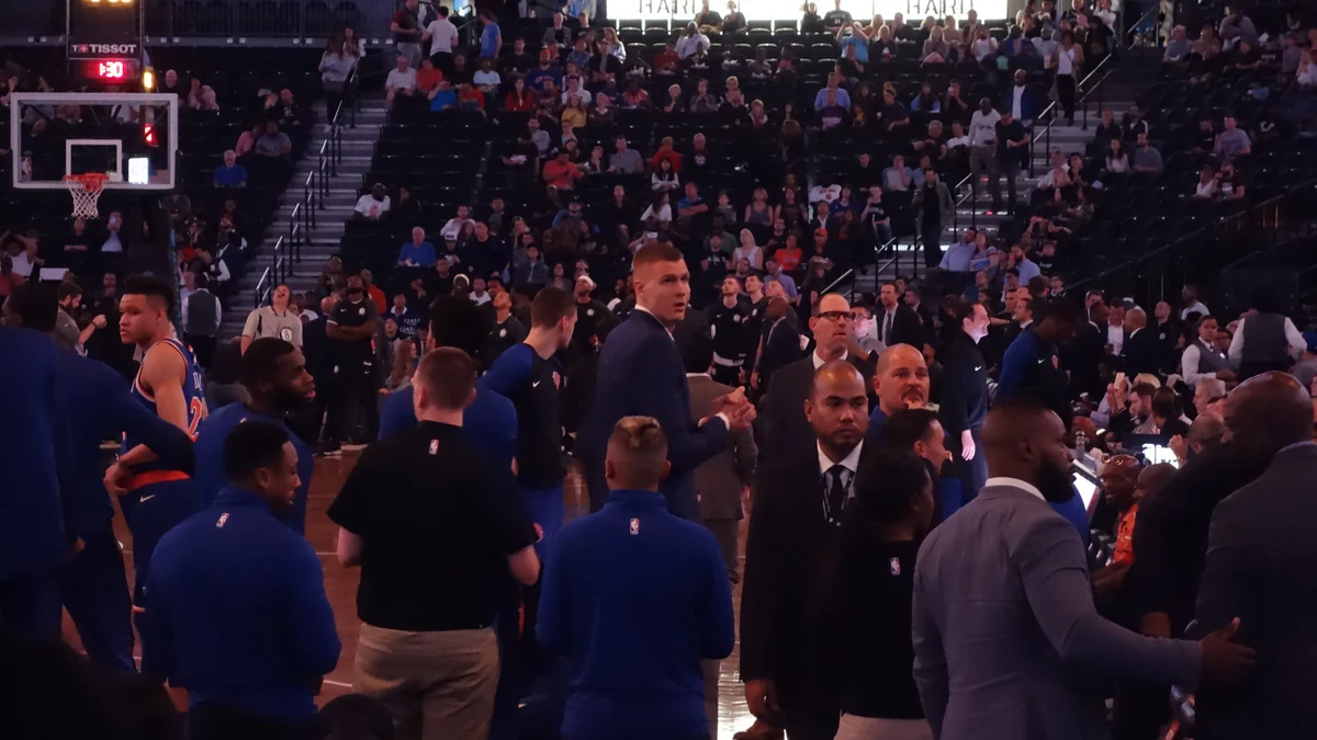 Jugadores e integrantes de los equipos reunidos junto a la cancha antes de un partido de baloncesto