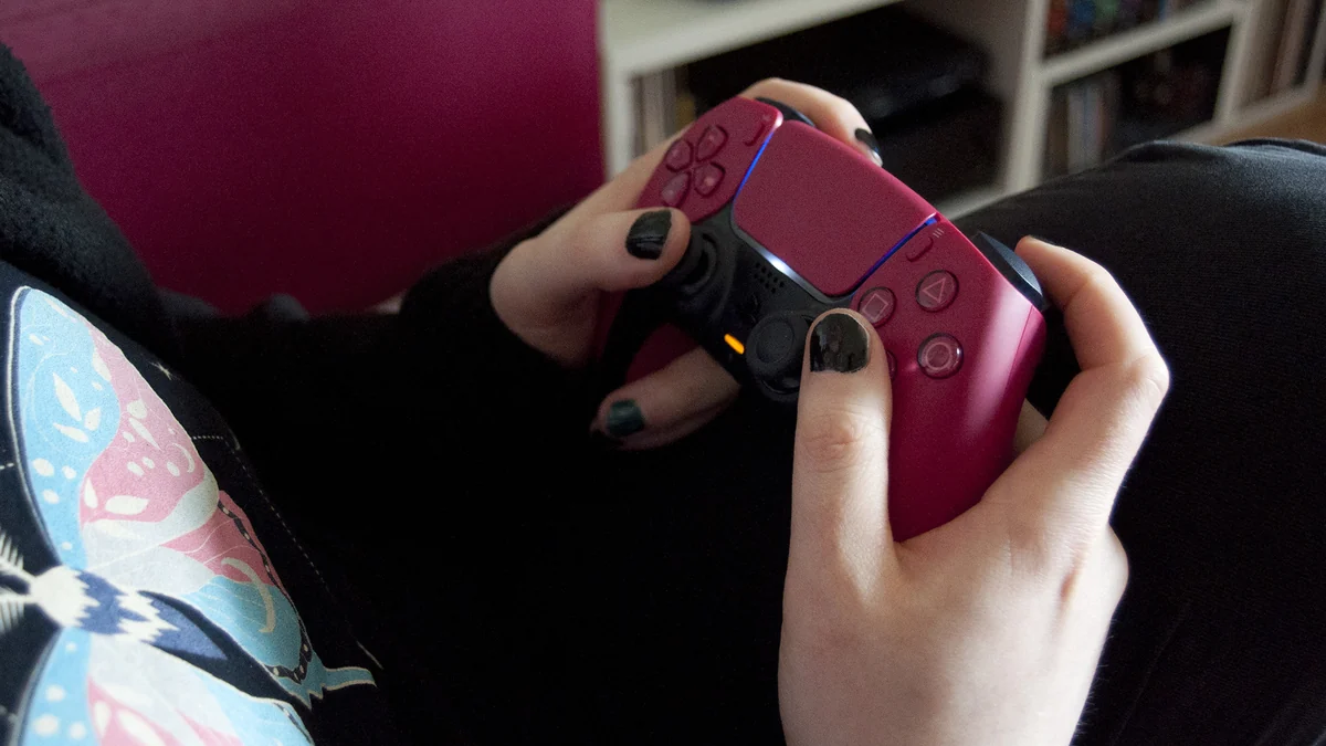 Mãos seguram um controle DualSense rosa com os polegares sobre os analógicos