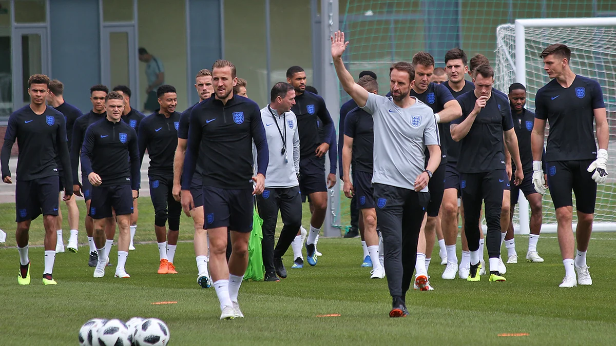 Jogadores e integrantes da comissão técnica da Inglaterra caminham juntos em um campo de treinamento.