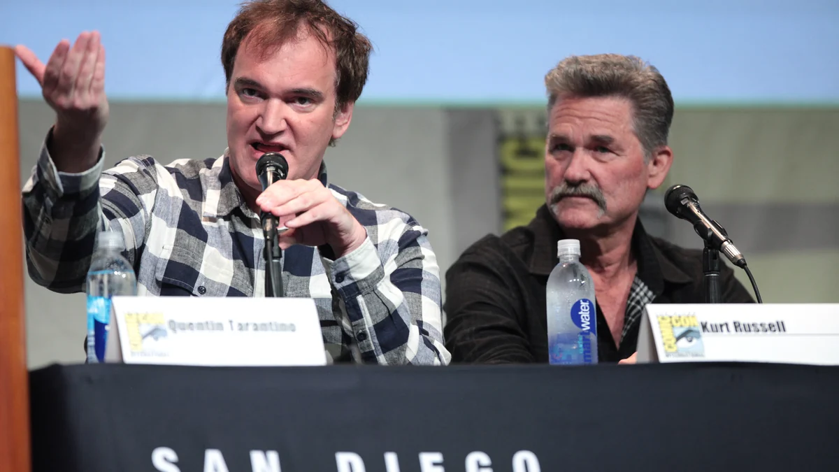 Quentin Tarantino speaks into a microphone as Kurt Russell watches him during a panel
