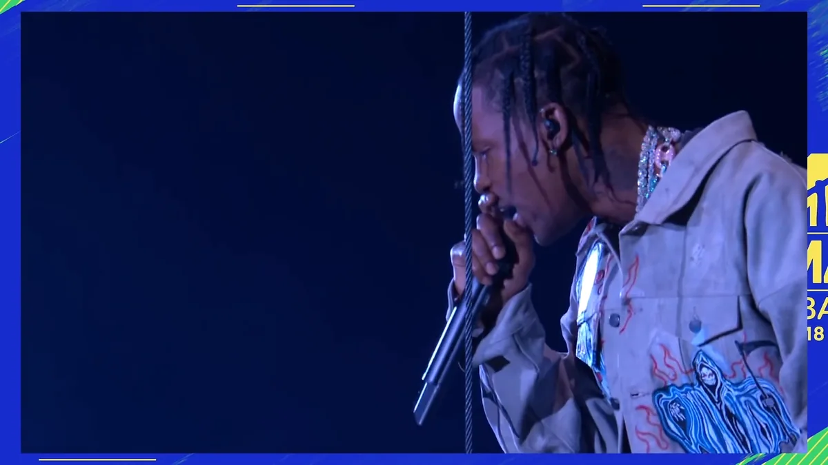Travis Scott canta con un micrófono en un escenario iluminado de azul