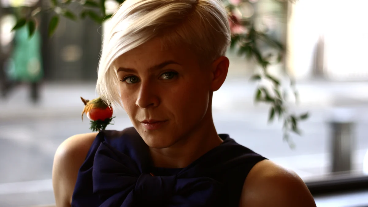 Robyn, con el pelo rubio corto, mira a la cámara con un pequeño pájaro en el hombro