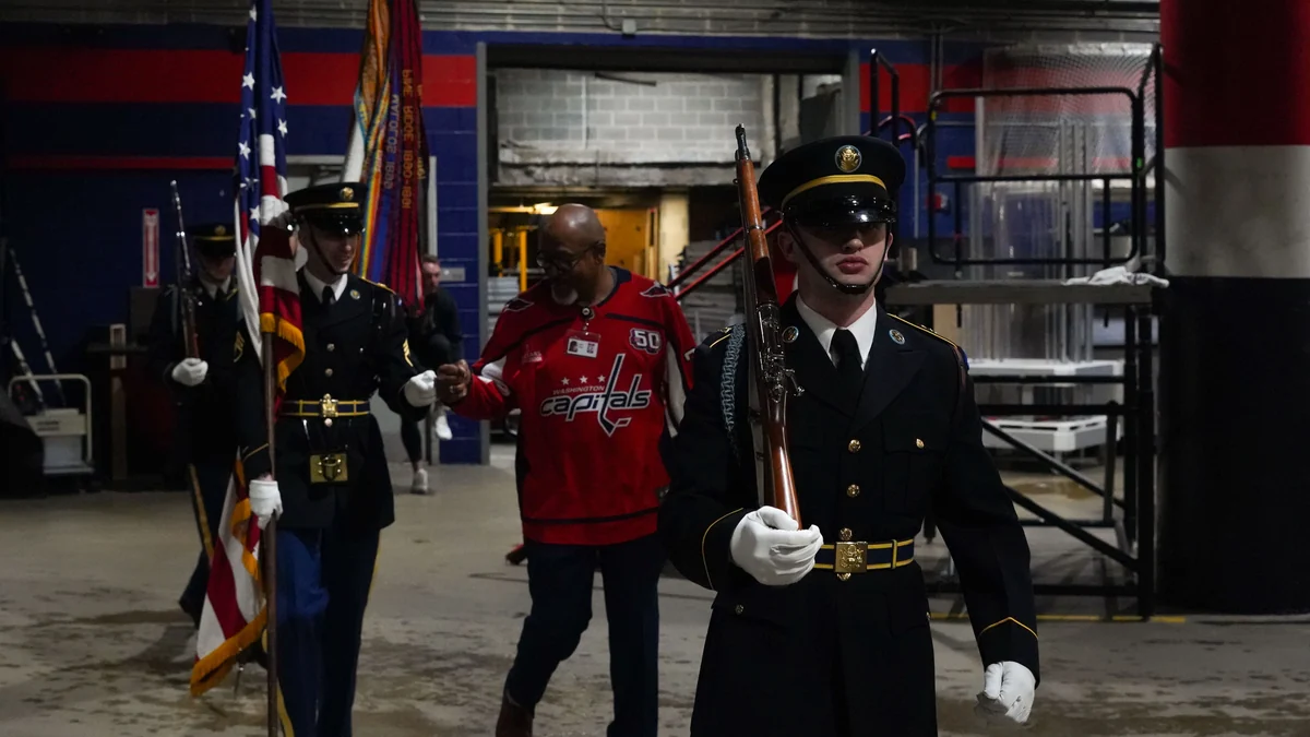 Militares em formação caminham por área interna da arena ao lado de homem com camisa dos Capitals.