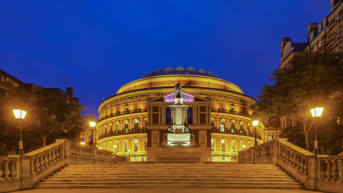 Royal Albert Hall illuminé de nuit derrière un escalier et un monument