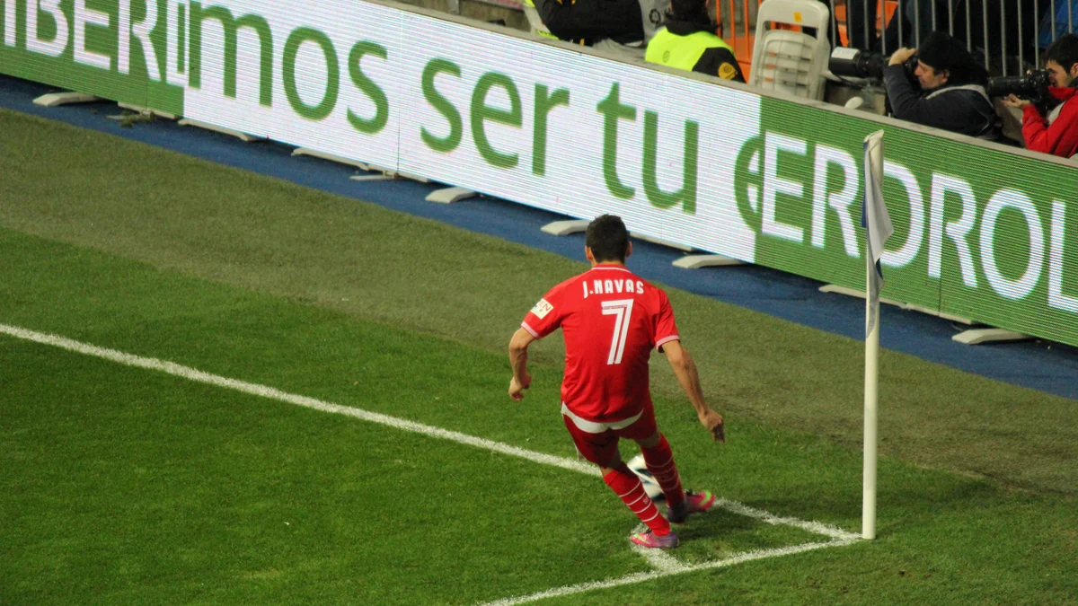 Jugador del Sevilla lanza un córner con uniforme rojo