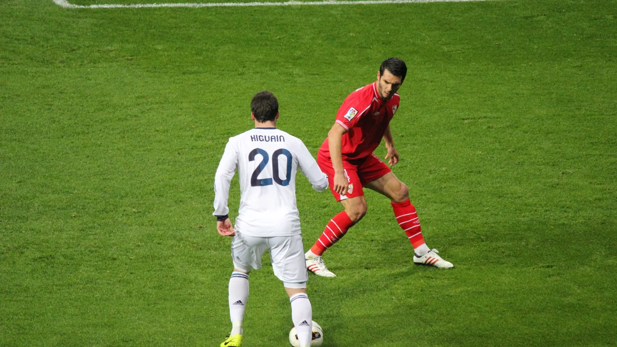 Jugador del Real Madrid con el balón frente a un rival del Sevilla