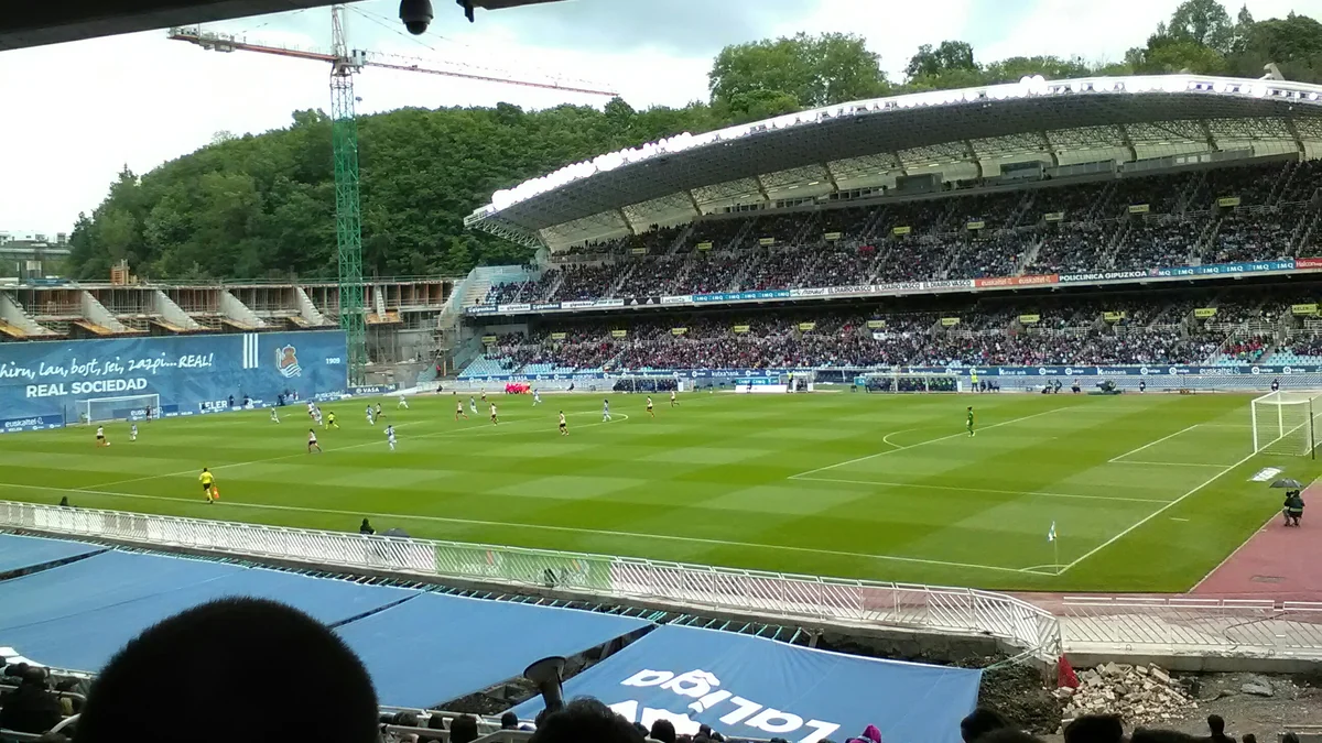 Wide view of a stadium during a women’s football match, with spectators in a covered stand