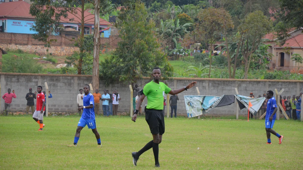 Referee in a green shirt points to the side as players wait on the pitch