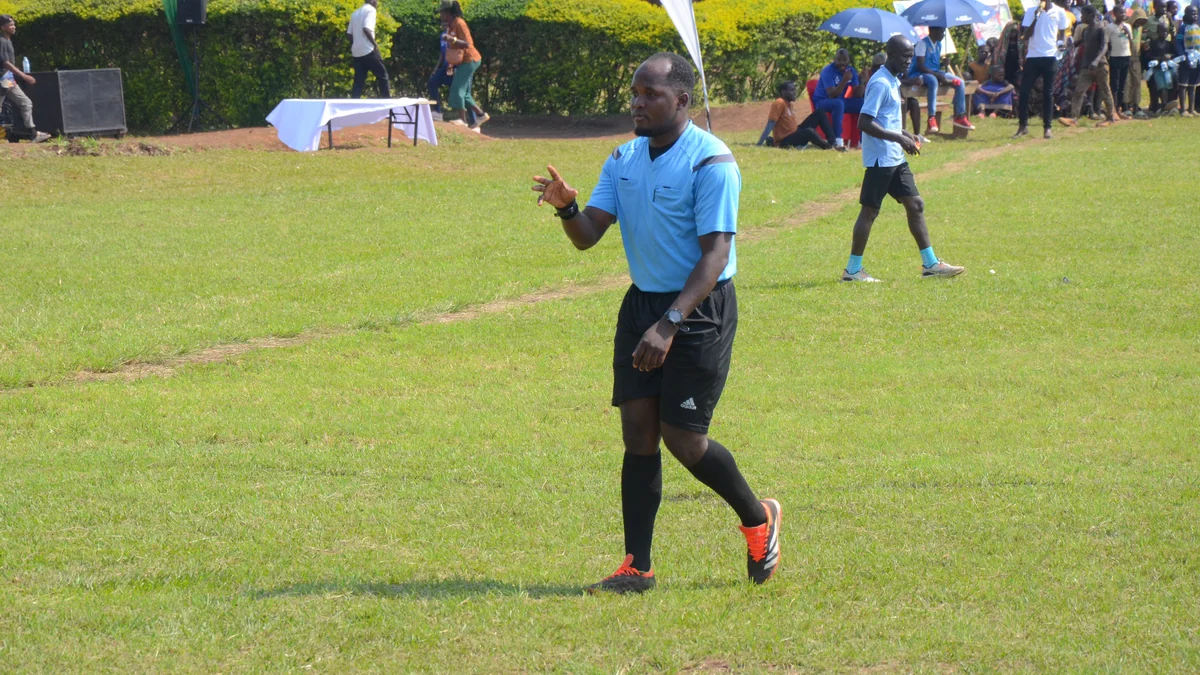 Referee in a blue shirt walks across the pitch while making a hand gesture