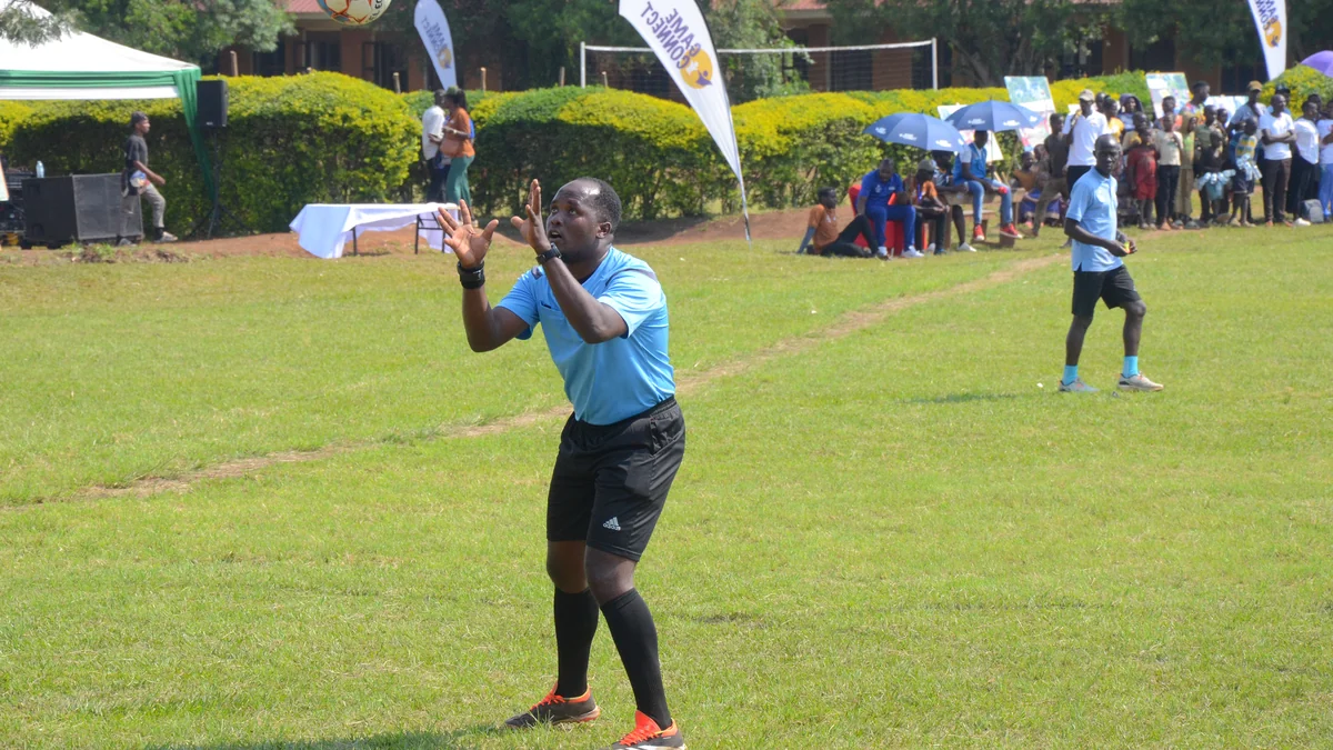 Referee in a blue shirt watches a ball overhead with both hands raised