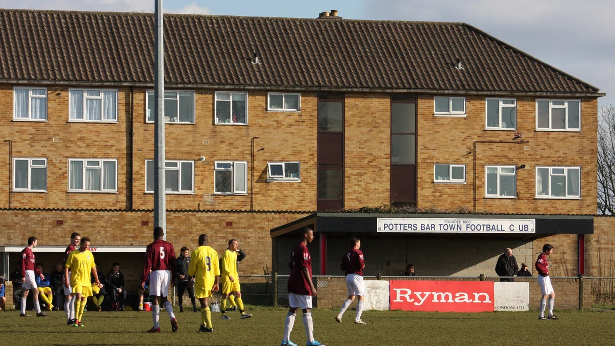Players in claret and yellow kits on the pitch in front of the Potters Bar Town Football Club stand
