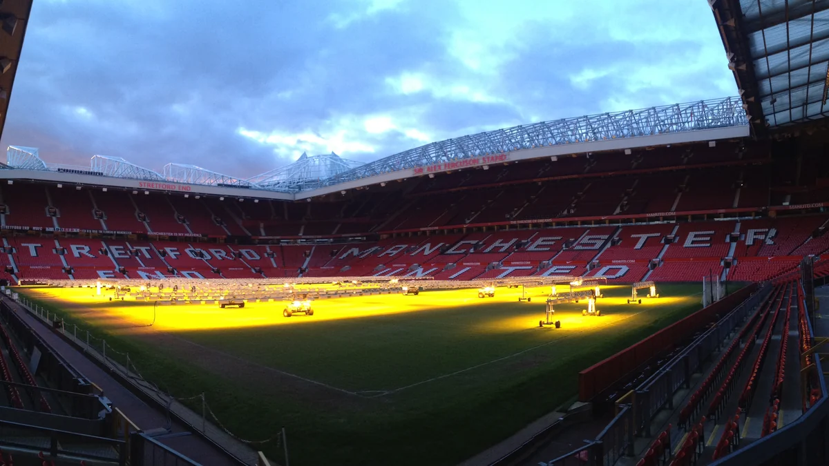 Arquibancadas vermelhas vazias e gramado iluminado dentro do estádio Old Trafford.
