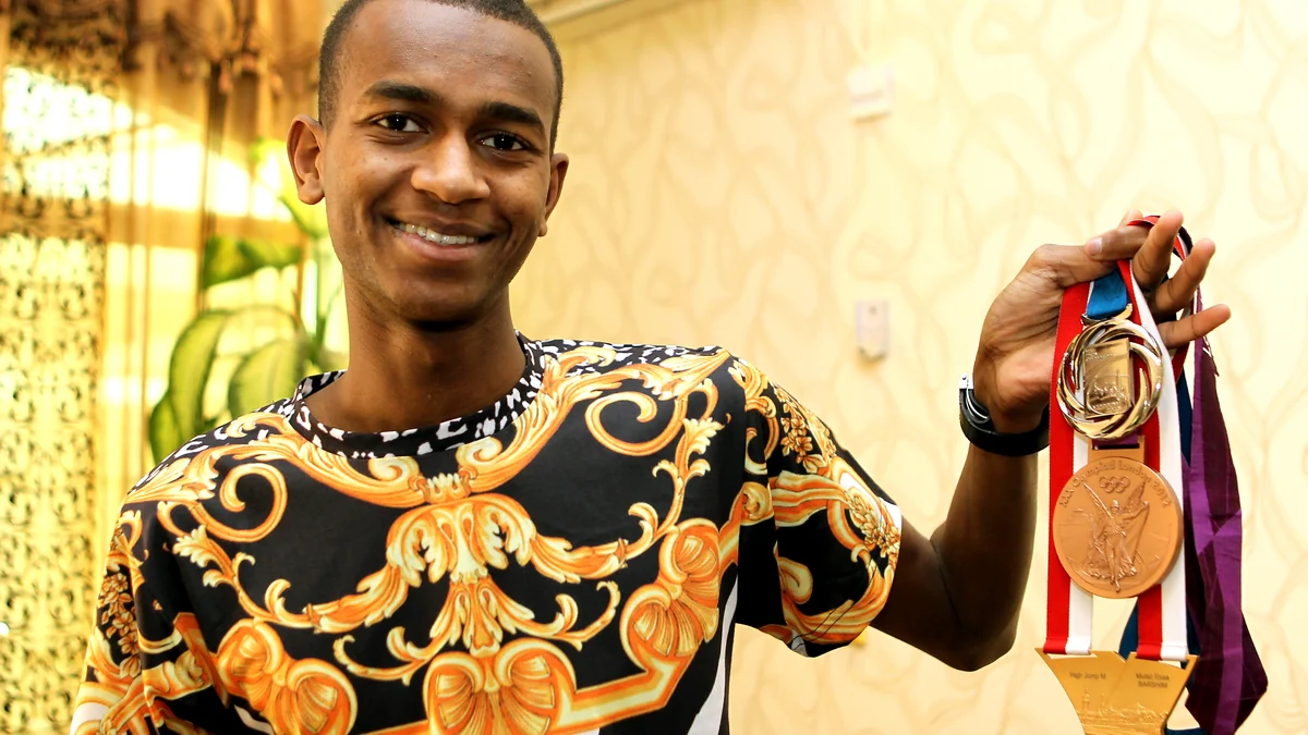 Mutaz Essa Barshim smiles while holding several medals by their ribbons