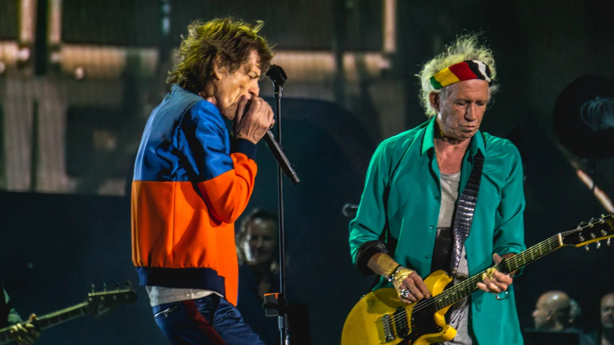 Mick Jagger sings into a microphone while Keith Richards plays a yellow guitar onstage