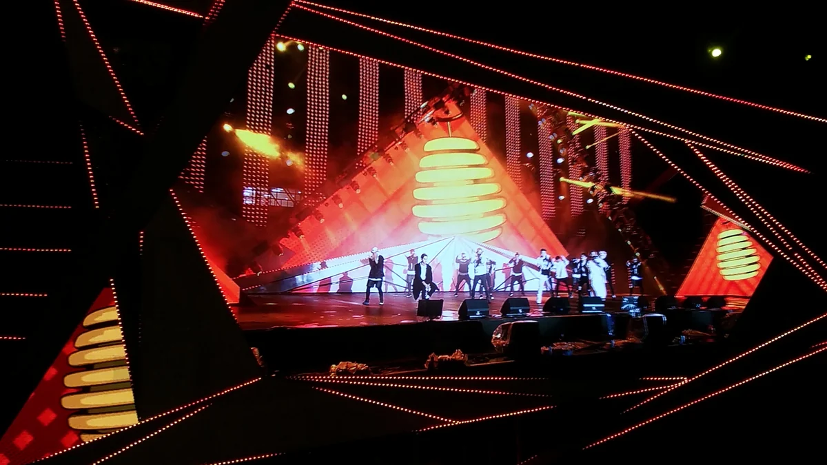 Groupe d’artistes sur une scène triangulaire éclairée en rouge