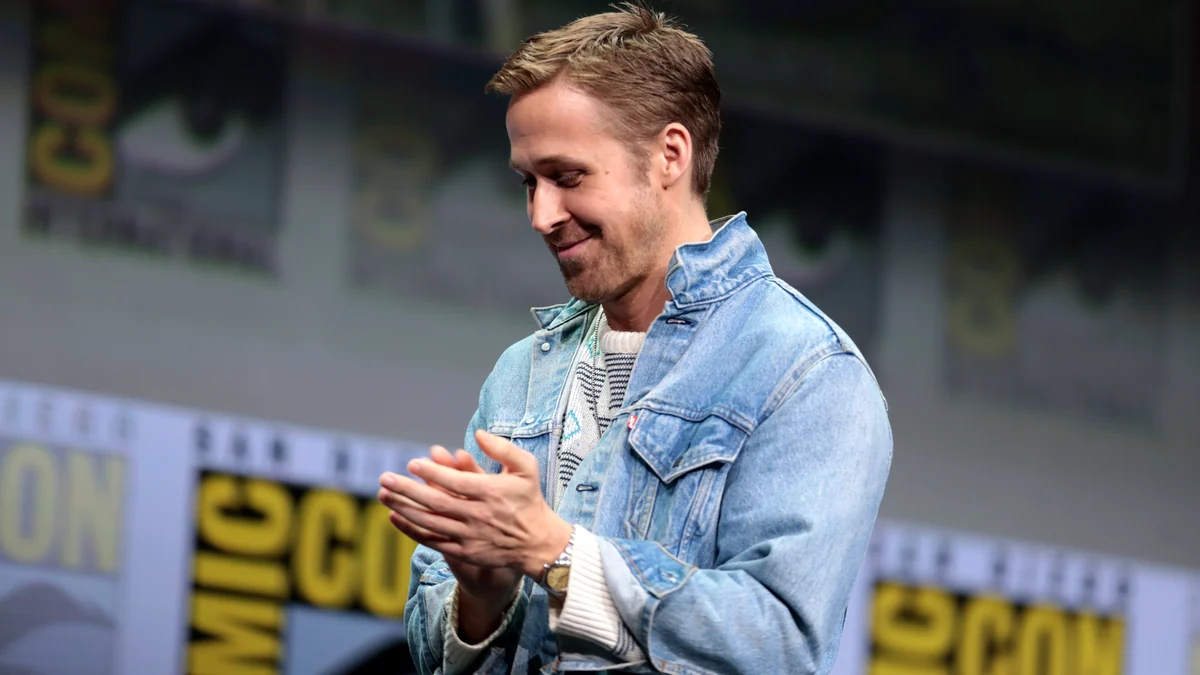 Ryan Gosling aplaudindo no palco, com jaqueta jeans clara
