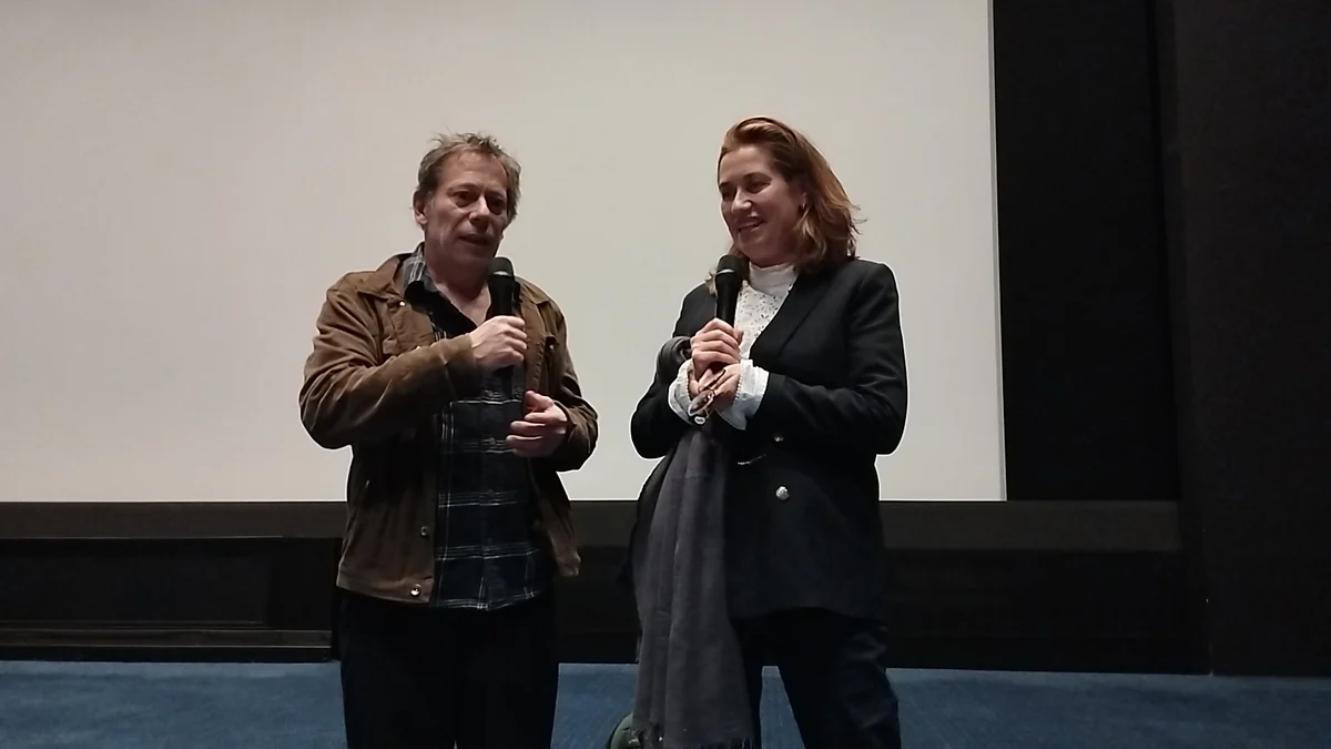 Mathieu Amalric y Emmanuelle Devos de pie ante una pantalla de cine, ambos con micrófonos.