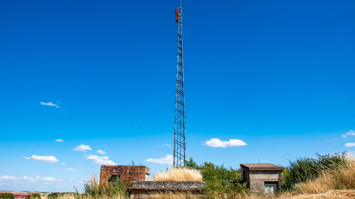 Torre alta de repetidor de TDT junto a pequenas construções sob céu azul