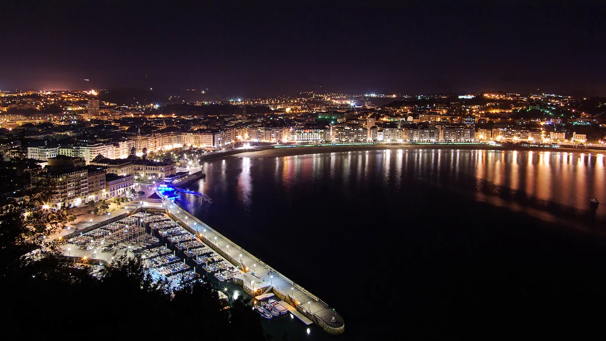 Night view of San Sebastián Bay, with the illuminated waterfront and a marina in the foreground