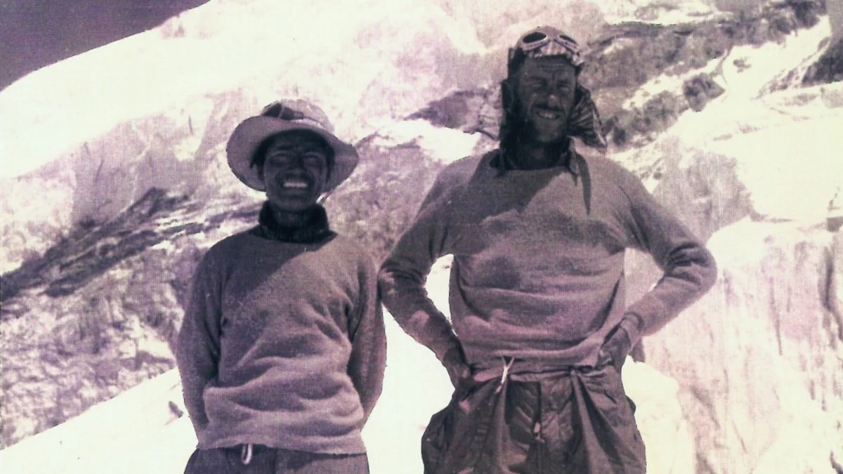Tenzing Norgay and Edmund Hillary in mountaineering clothes against a snowy landscape