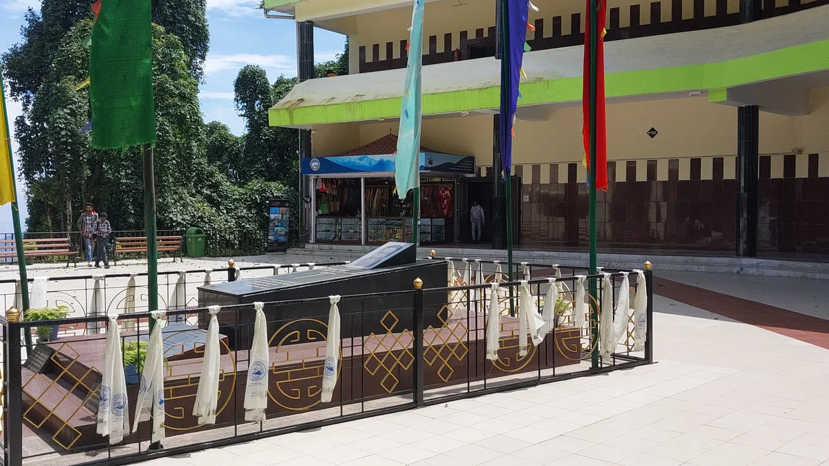Dark grave surrounded by a railing and vertical flags at the Tenzing Memorial in Darjeeling