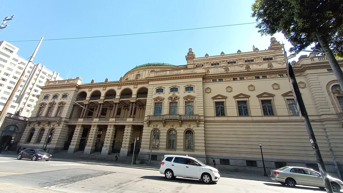 Fachada clara y ornamentada del Theatro Municipal vista desde el otro lado de la calle, con automóviles en primer plano.