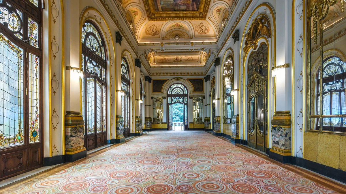 Galería interior con vitrales, puertas de madera, ornamentos dorados y piso de motivos circulares.