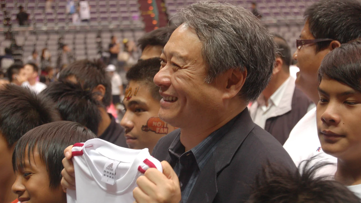 Ang Lee smiles in a crowded area while holding a white shirt