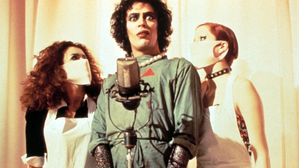 Tim Curry as Dr. Frank-N-Furter at a microphone in The Rocky Horror Picture Show.